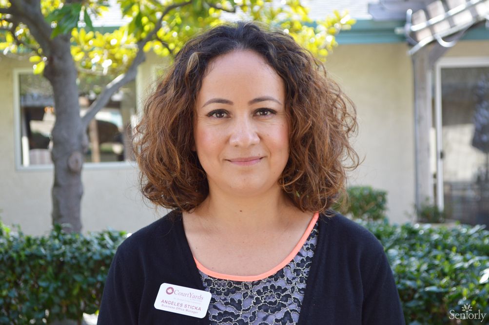 A woman with curly hair is smiling outdoors.