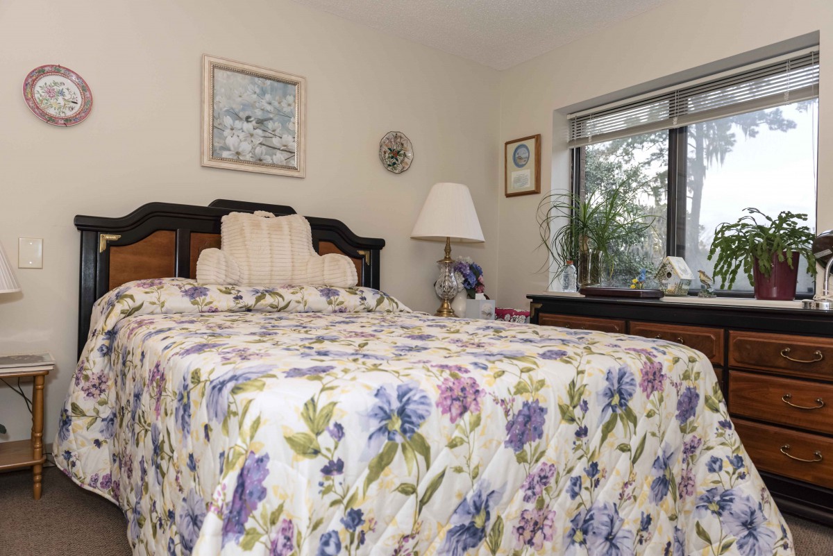 A cozy bedroom with a floral bedspread and decorative elements by the window.