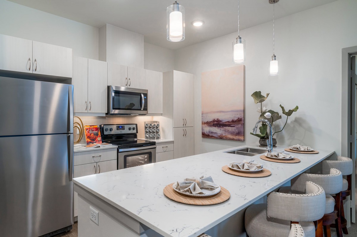 A modern kitchen with stainless steel appliances, a central island with bar stools, and pendant lighting.