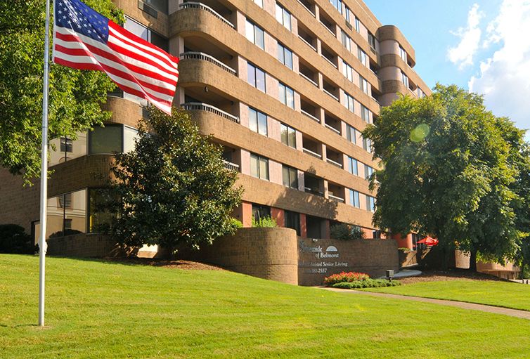 A multi-story apartment building with a well-manicured lawn and an American flag flying in front.