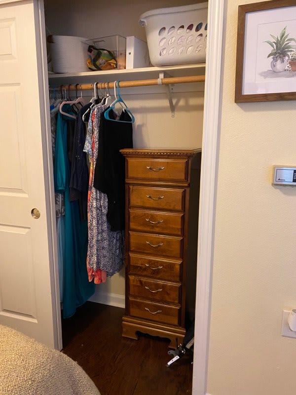 A closet with hanging clothes and a wooden chest of drawers.