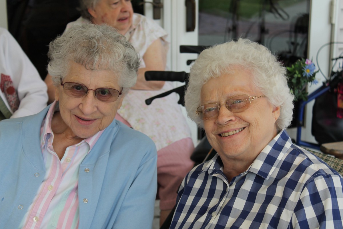 Two elderly women sitting together and smiling outdoors.