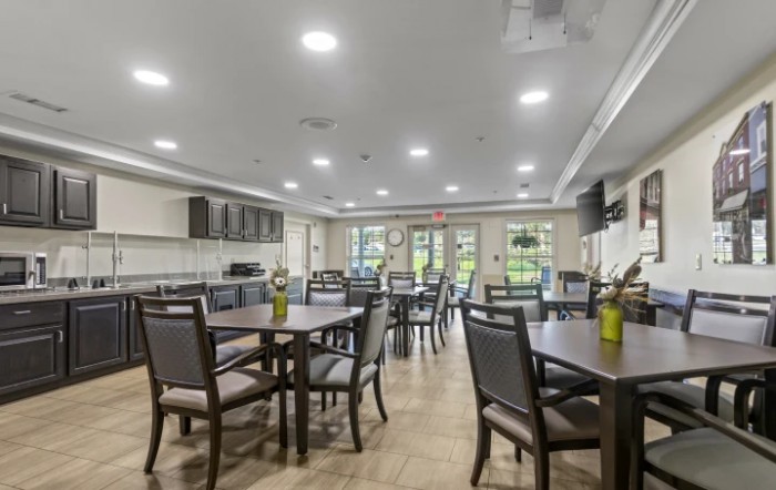 A modern dining area with multiple tables and chairs, well-lit and featuring a kitchen setup.