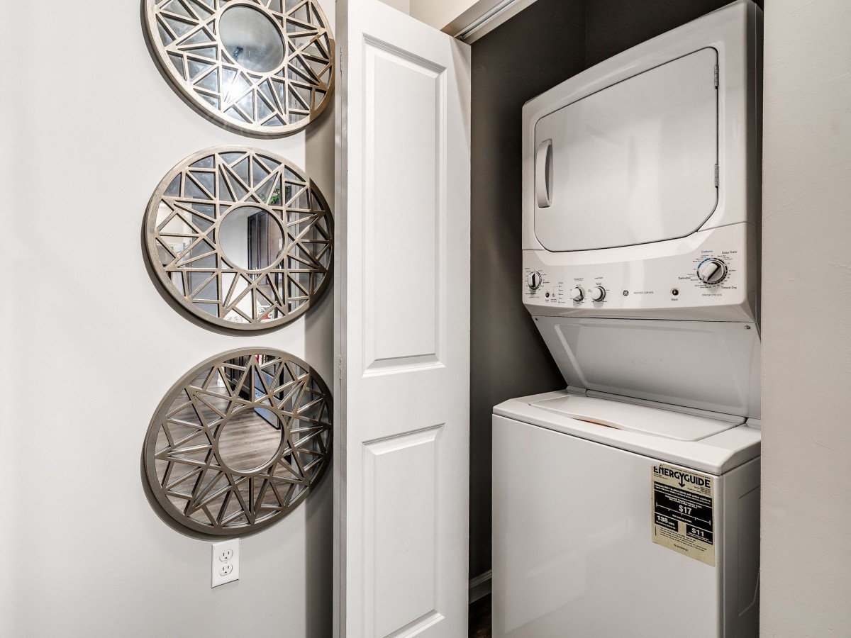 A compact laundry room with a stacked washer and dryer next to decorative mirrors.