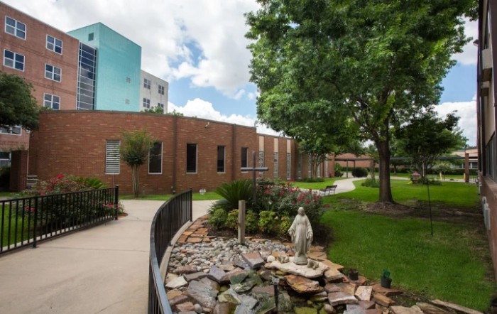 A peaceful garden with a statue and pathway beside a brick building.