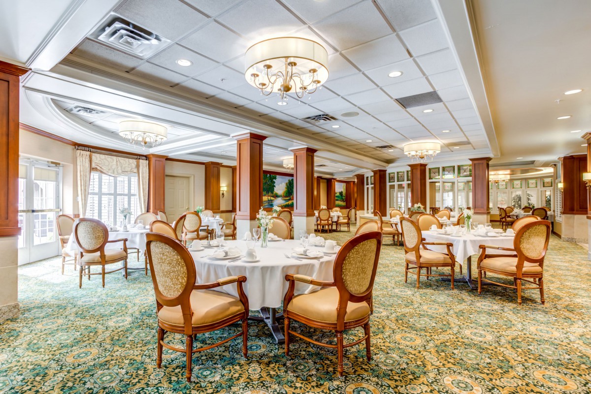 An elegant dining room with round tables, upholstered chairs, and chandeliers.