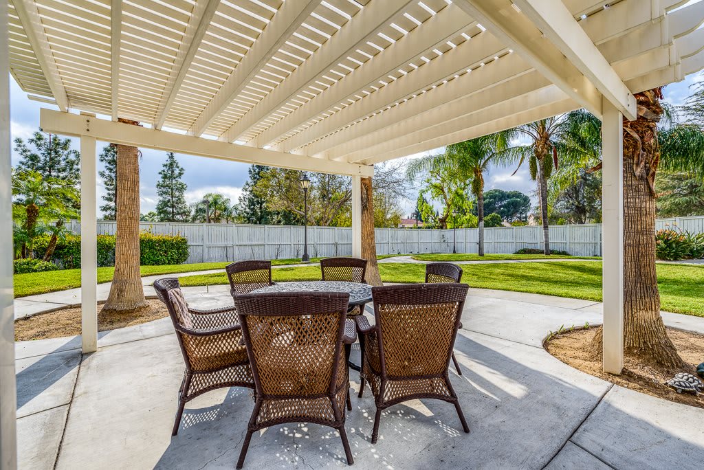 A spacious outdoor patio with wicker furniture under a pergola, surrounded by greenery.