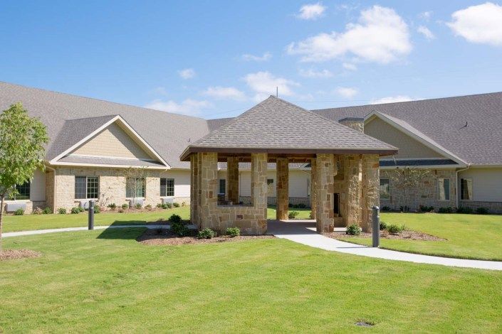 A beautiful, sunny day at a modern building with a stone gazebo and well-maintained lawn.