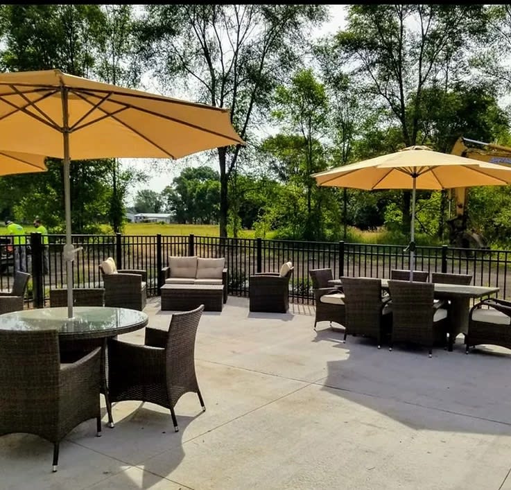 A tranquil outdoor patio with tables and chairs under large umbrellas, surrounded by trees on a sunny day.