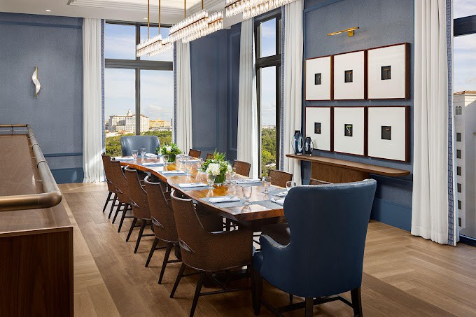 A beautifully designed dining room with a large table, elegant chairs, and decor elements such as artwork and expansive windows.