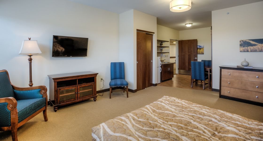A modern bedroom interior featuring a TV, chairs, and cozy decor.