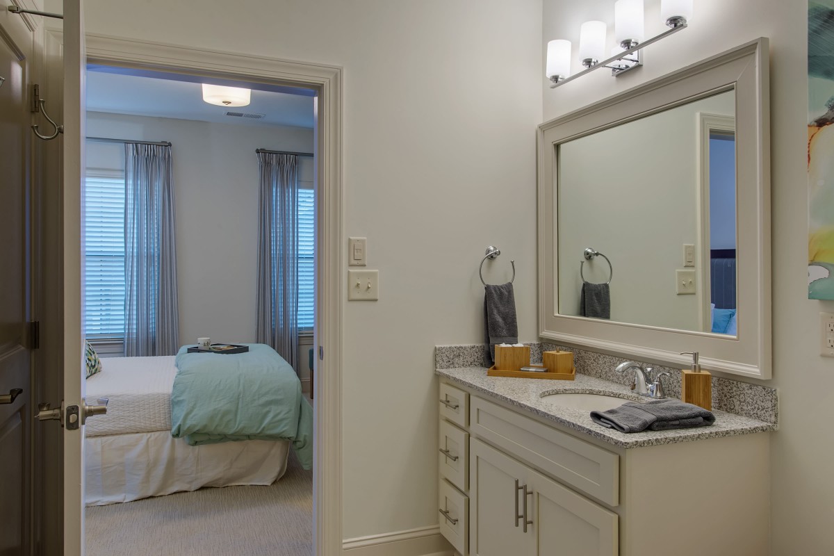 A view from the bathroom into a cozy bedroom, featuring a well-lit vanity area.
