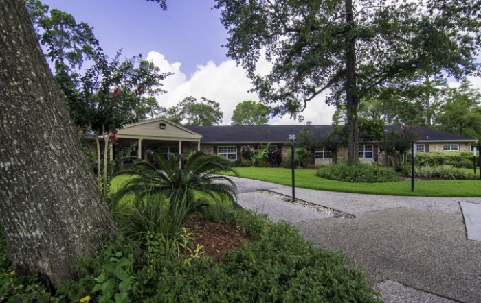 A picturesque view of a residential house with a driveway surrounded by lush landscaping and trees.