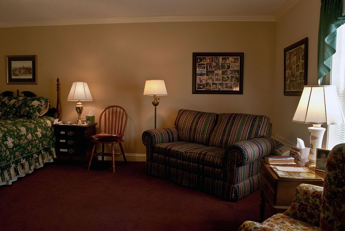 A cozy living room featuring a striped sofa, wooden chair, and lamps with warm lighting.