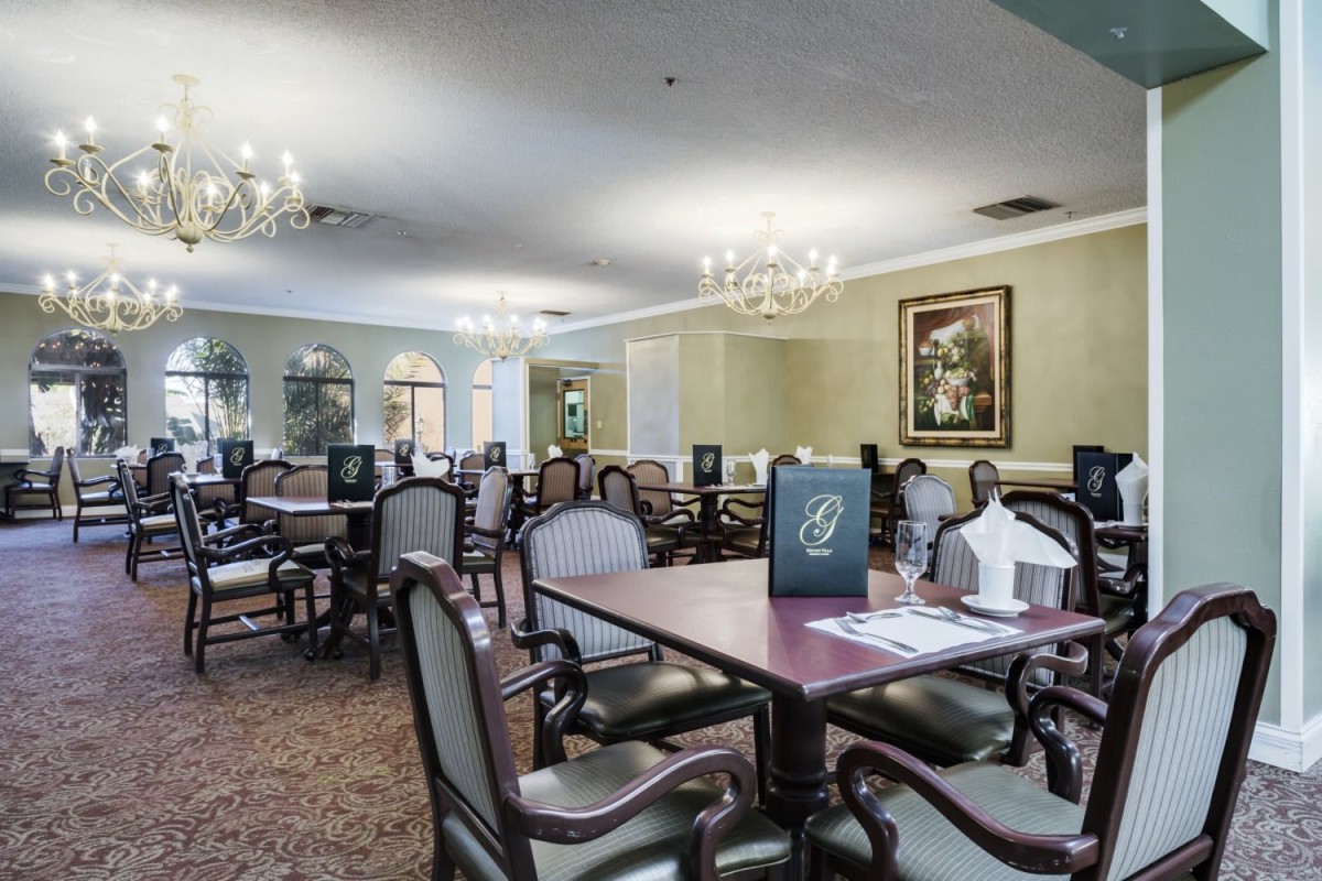 A spacious dining room with elegant chandeliers and neatly arranged tables and chairs.