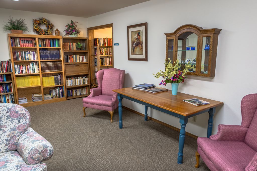 A cozy interior space with bookshelves, armchairs, and a decorative table with flowers.