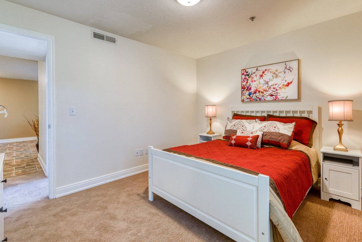 A cozy bedroom featuring red bedding, a stylish lamp, and art on the wall.