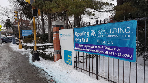 A sign announcing the upcoming opening of Spaulding Rehabilitation in Brighton, set against a snowy backdrop.