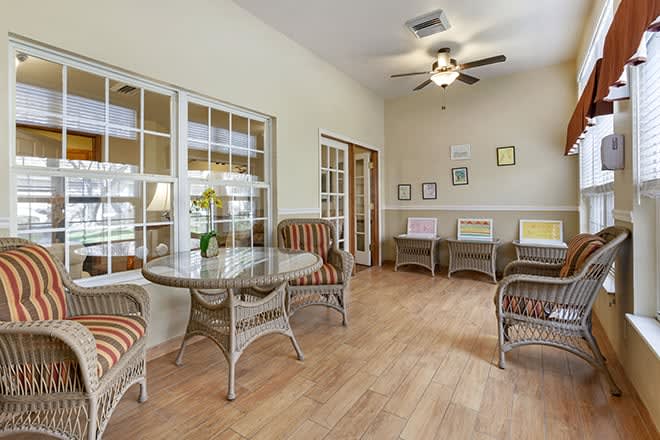 A cozy living room with wicker furniture, large windows, and a ceiling fan.