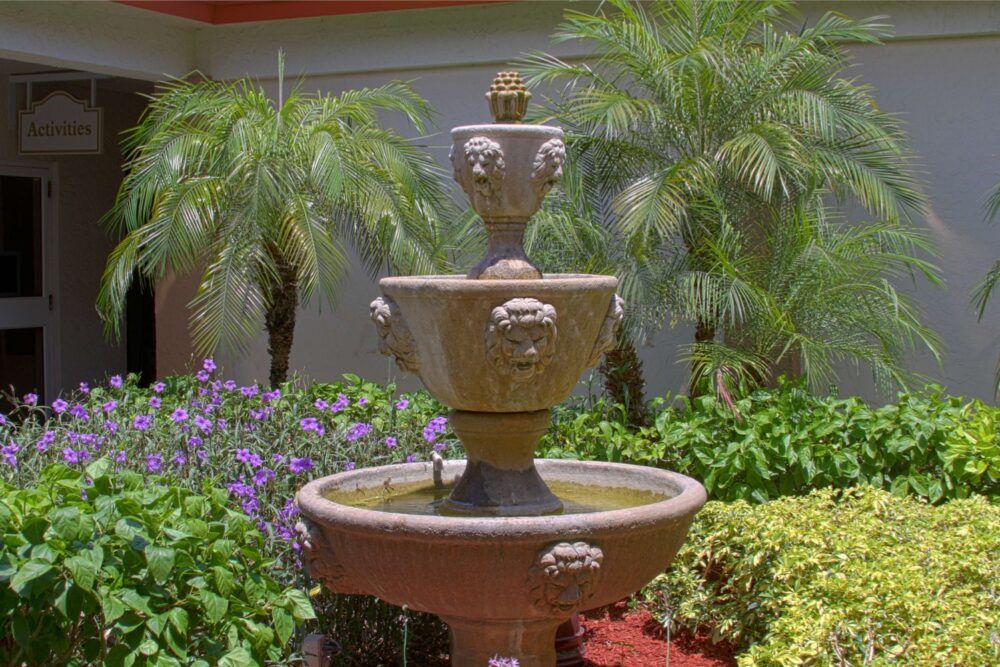 A decorative tiered fountain surrounded by lush greenery and vibrant flowers in a serene garden setting.