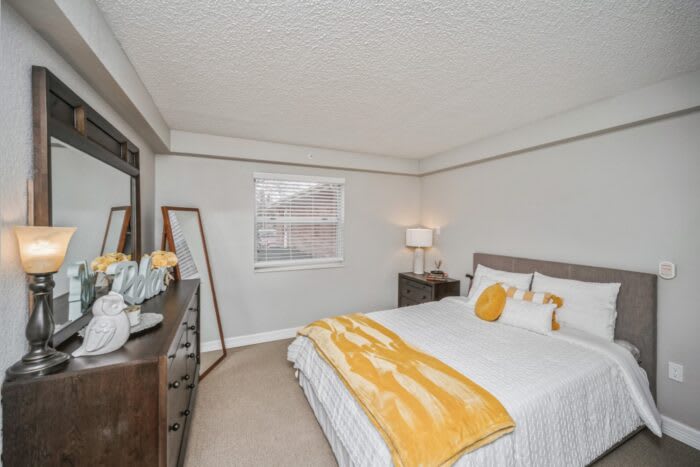 A modern bedroom with neutral tones and yellow accents, featuring a large bed, a mirror, and stylish decor.
