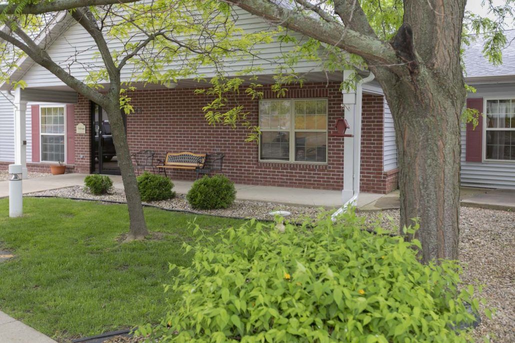 A suburban house with a brick exterior, featuring a porch swing and surrounded by trees and bushes.