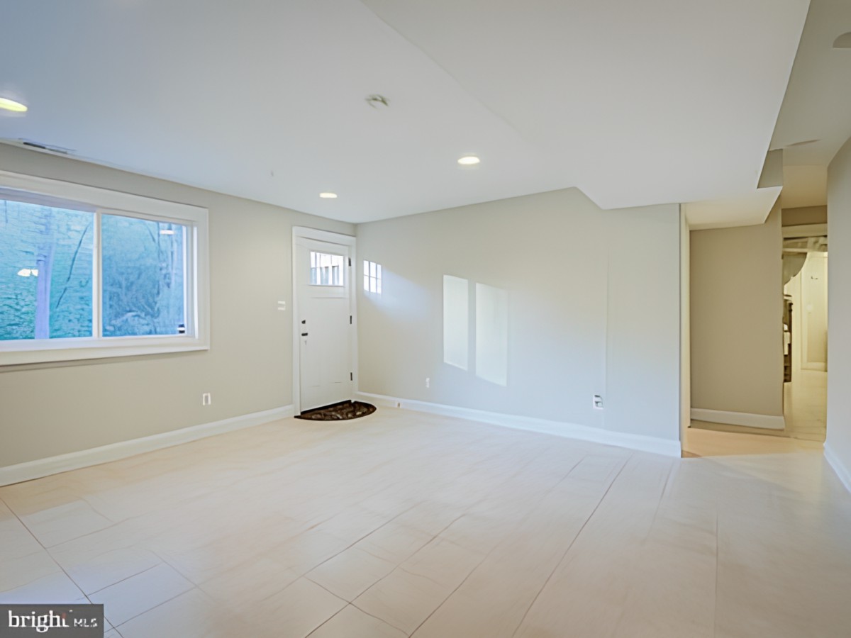 A spacious, empty basement with neutral-colored walls and carpet, featuring recessed lighting and a window with natural light.