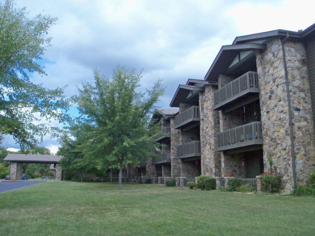 Stone facade apartment buildings with balconies, surrounded by trees on a cloudy day.