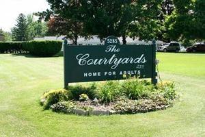 Sign indicating 'The Courtyards' home for adults, surrounded by landscaping and greenery.
