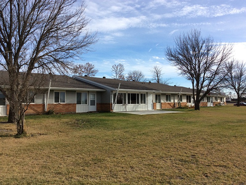 A suburban single-story house with a lawn and trees under a blue sky.