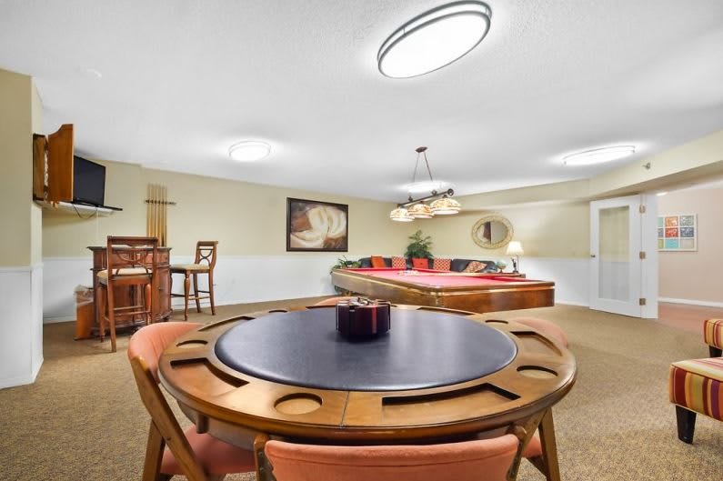 A spacious game room featuring a pool table and card table with ample seating.
