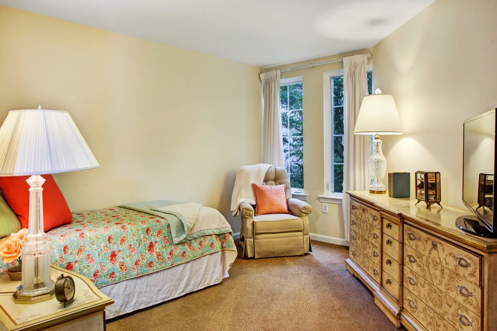 A cozy bedroom with a comfortable bed, armchair, and warm lighting.