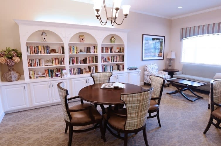 A cozy reading room with bookshelves, a round table, and chairs.