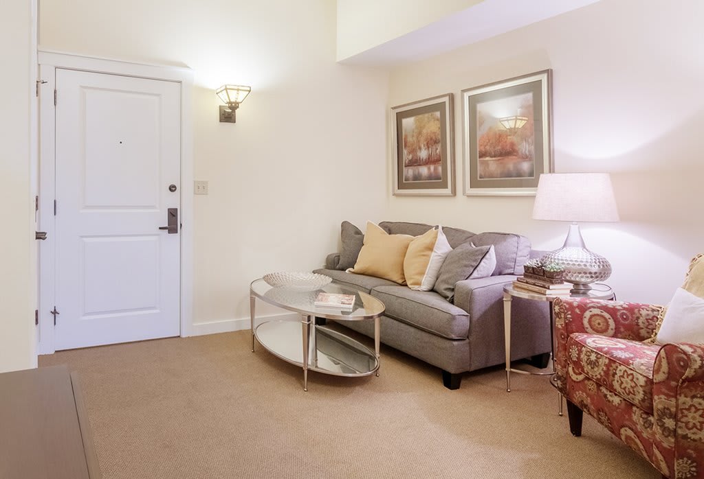 A cozy living room with a comfortable sofa, glass coffee table, and warm lighting.