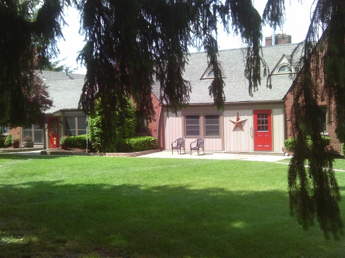 A quaint house with a lush green lawn and trees in the foreground.