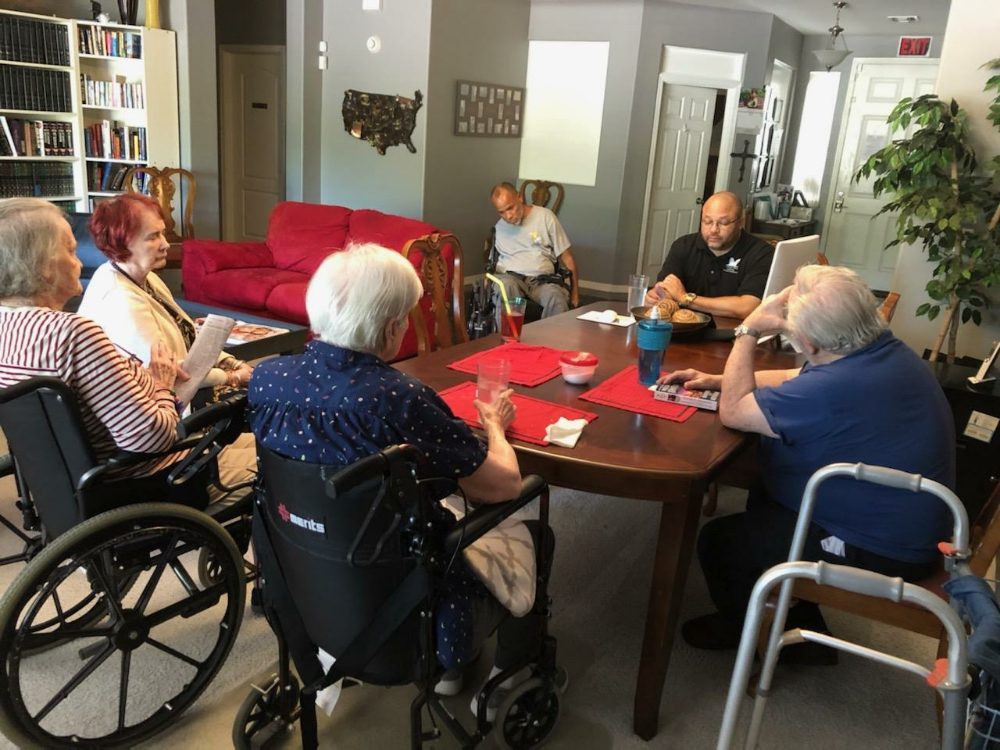 A group of elderly individuals sitting around a table in a care home, engaging in conversation.