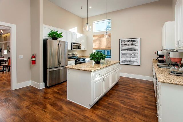 A modern kitchen featuring stainless steel appliances, a large island with pendant lighting, and wood flooring.