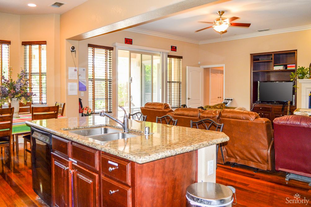 A spacious open floor plan kitchen and living area with granite countertops, wooden cabinets, and abundant natural light.