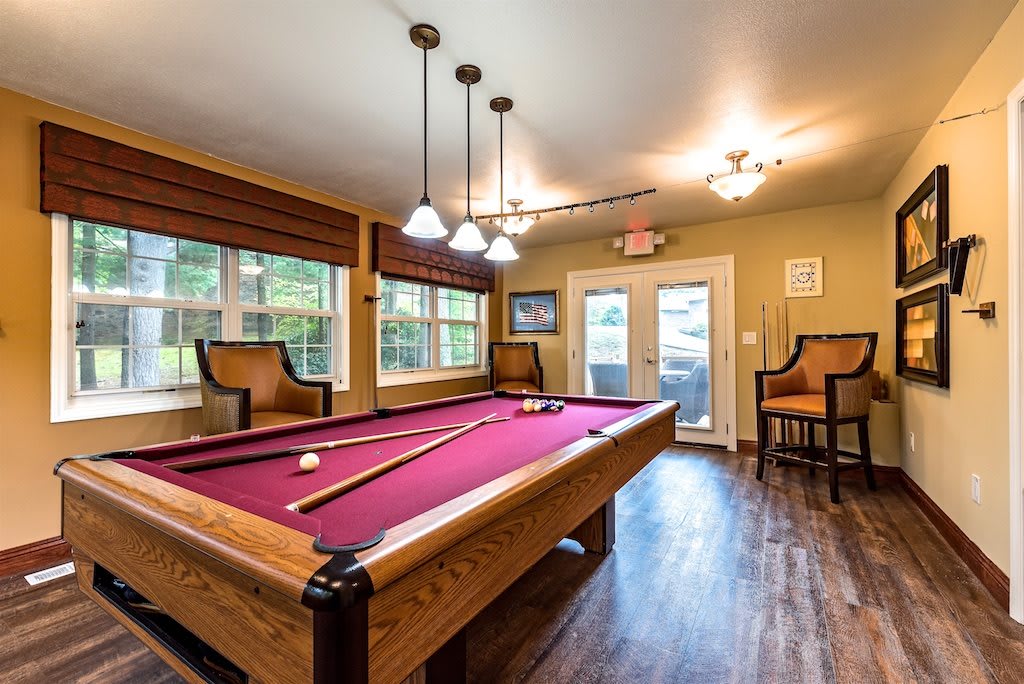 A cozy billiards room featuring a pool table with red felt, stylish lighting fixtures, and comfortable seating.