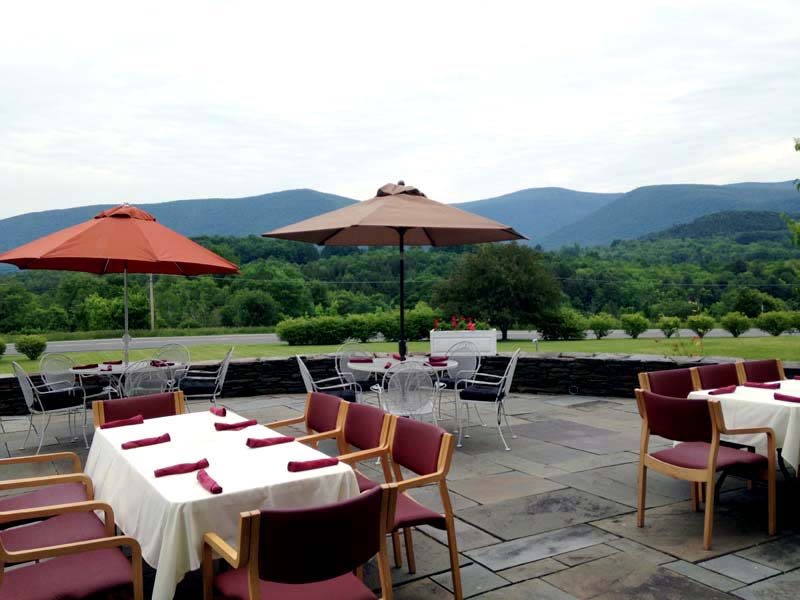 A picturesque outdoor dining area set against a backdrop of rolling mountains with neatly arranged tables and umbrellas.