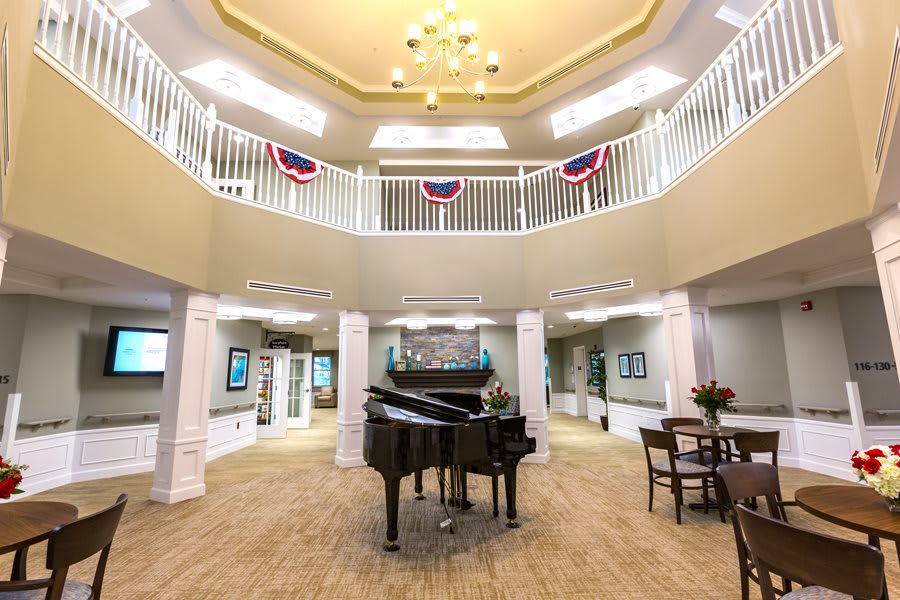 A spacious lobby with a grand piano and elegant chandelier, featuring a balcony adorned with decorative banners.