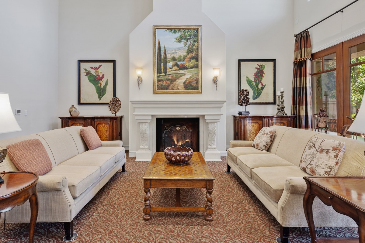 A traditionally styled living room featuring two sofas, a central fireplace adorned with art, and a wooden coffee table.