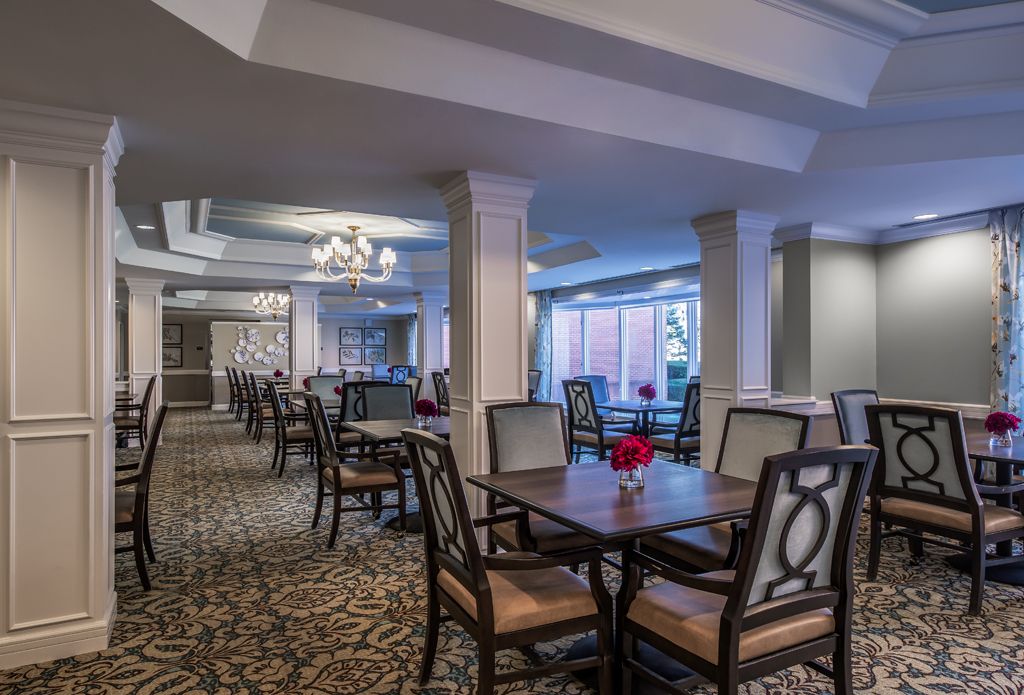 An elegant dining room with neatly arranged tables and chairs, featuring a chandelier and carpeted flooring.