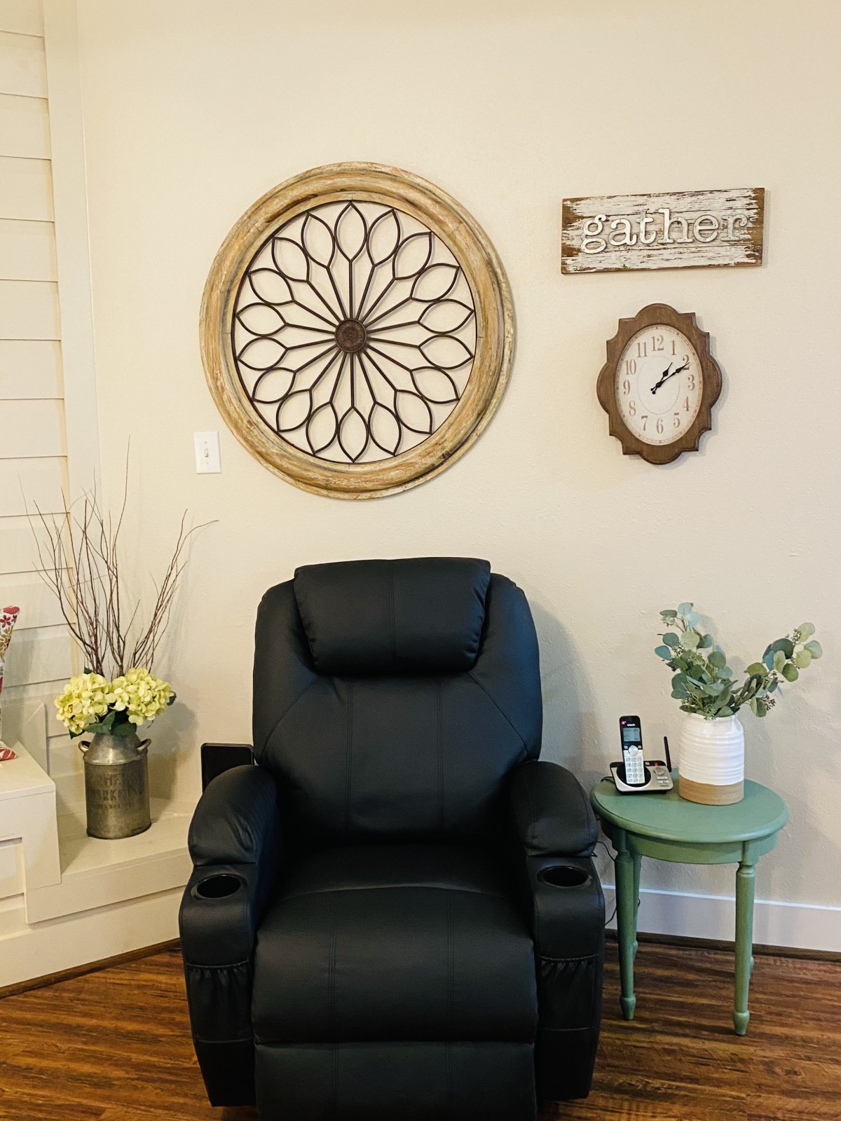 A cozy living room corner featuring a black recliner, wall art, and a side table with plants.