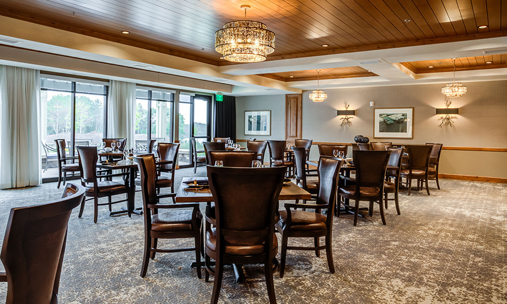 An elegant dining area with wooden tables and chairs, featuring a decorative chandelier.