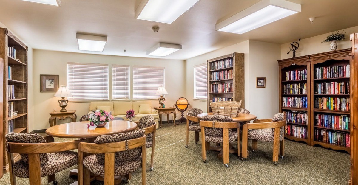 A cozy living room featuring tables, chairs, a bookshelf, and a lamp.