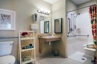 A clean and modern bathroom with a sink, mirror, shelf, and accessible shower.