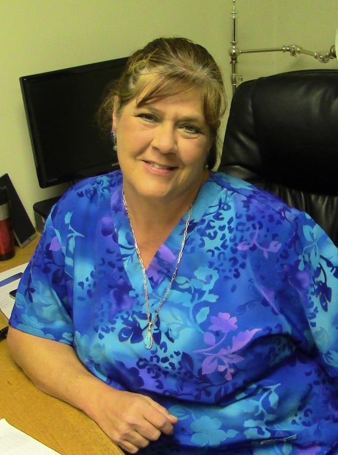 A woman smiles while seated at a desk in an office.