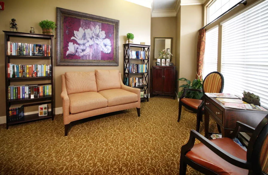 A cozy living room with a sofa, bookshelves, and floral artwork.