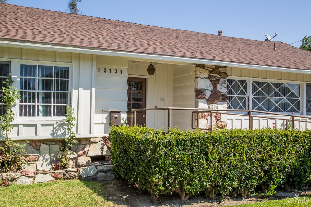 A cozy single-story house with a small porch and neatly trimmed hedge in the front yard.